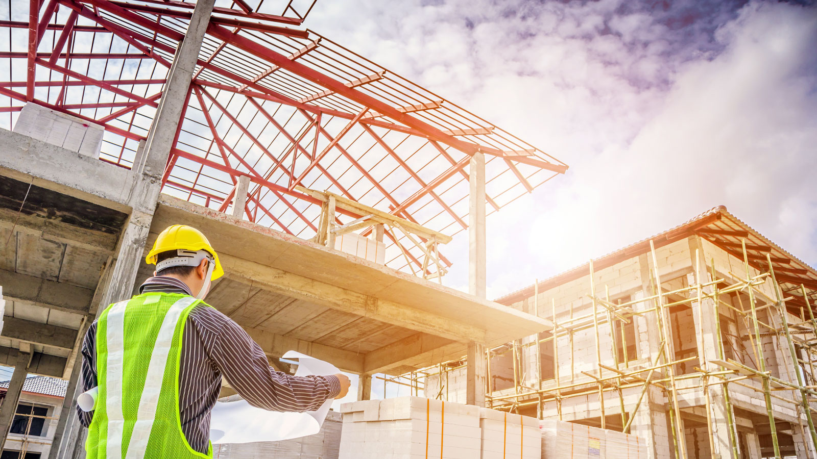 A professional engineer in safety helmet holding blueprints at a house construction site, inspecting a residential house under construction.